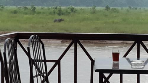 a table and chairs with a glass of beer on a balcony at Jungle Wildlife Camp in Sauraha