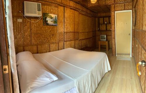 a bedroom with a white bed in a wooden wall at Bamboo House Beach Lodge & Restaurant in Puerto Galera