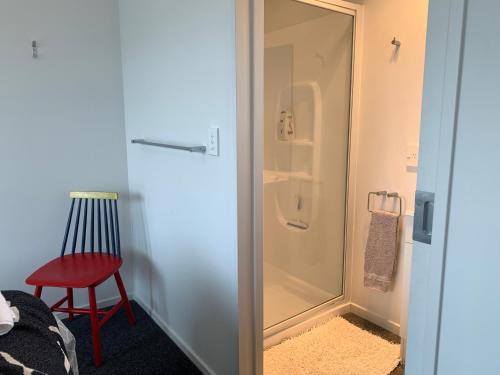 a glass shower door in a room with a red chair at A Beauty on Bligh St Te Anau in Te Anau
