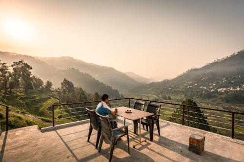 a man sitting at a table overlooking a valley at Odyssey Stays Kausani in Kausani