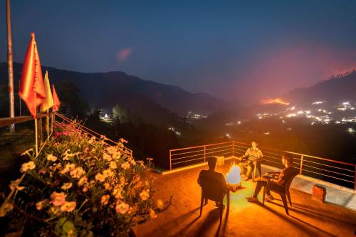 a group of people sitting around a fire at night at Odyssey Stays Kausani in Kausani