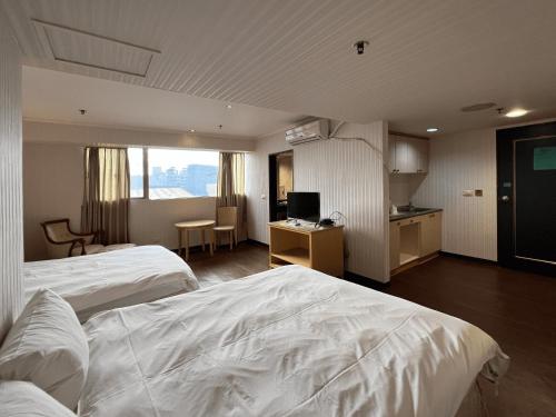 新竹市にあるエルメス ホテルの白いベッド2台とキッチンが備わるホテルルームです。