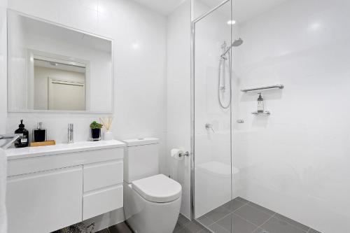a white bathroom with a toilet and a shower at The Beach Studio in Huskisson