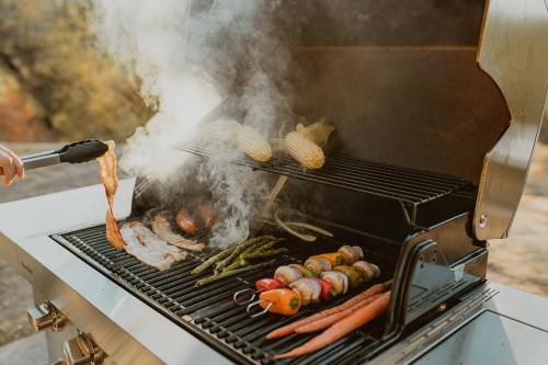 a person grilling meat and vegetables on a grill at Glamour Mountain Getaway by Casa Oso with views and spa in Oakhurst