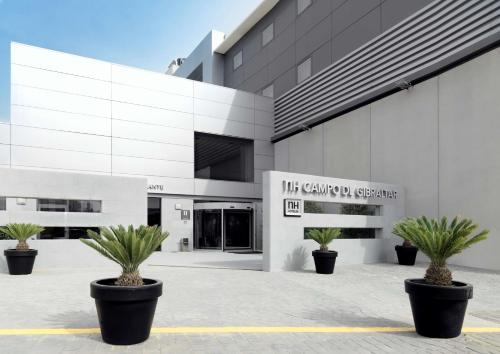 un edificio con due piante in vaso di fronte ad esso di NH Campo de Gibraltar a Los Barrios