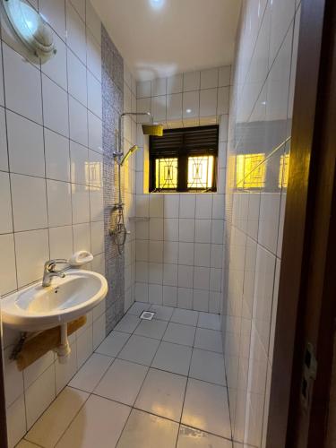 La salle de bains est pourvue de carrelage blanc, d'un lavabo et d'une fenêtre. dans l'établissement Farm Cottage, à Mukono