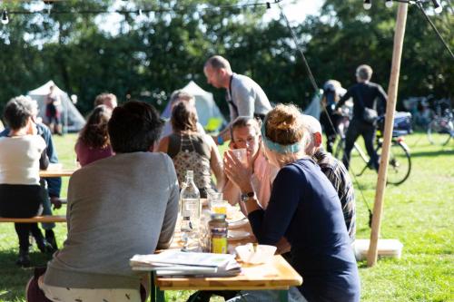een groep mensen die aan een picknicktafel zitten bij BlueCAMP Oerol24- Tent&Breakfast in West-Terschelling