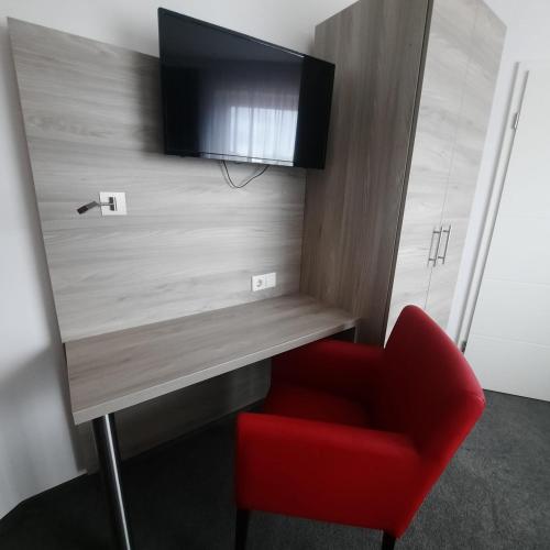 a red chair and a desk with a television on a wall at Eventhaus Schamin in Erpen