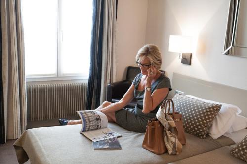 a woman sitting on a bed talking on a cell phone at Hôtel La Résidence du Berry in Versailles
