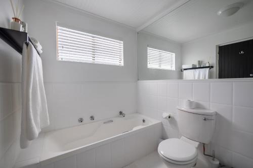 a white bathroom with a toilet and a bath tub at Bitou River Lodge in Plettenberg Bay