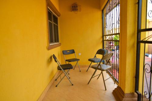 three chairs sitting on a balcony next to a yellow wall at Living Green APARTMENTS AIRPORT PICK UP in Benin City