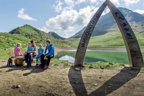 a group of children sitting on a bench next to a lake at Gaestehaus Berger in Sankt Jakob in Defereggen