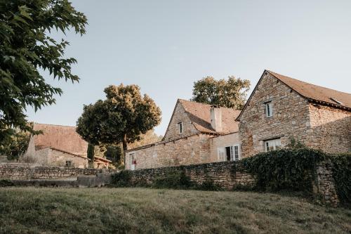 una antigua casa de piedra con una pared y árboles en Domaine St-Amand en Saint-Amand-de-Coly