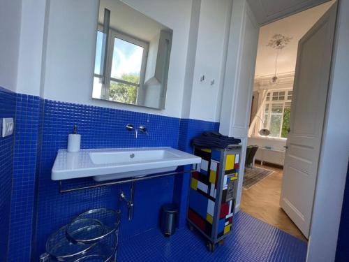 een blauw betegelde badkamer met een wastafel en een spiegel bij Suite Célestine Palace Excelsior vue lac in Aix-les-Bains