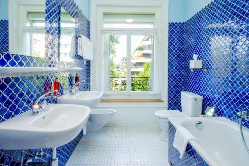 a blue tiled bathroom with two sinks and a toilet at Hotel Beau Séjour Lucerne in Luzern