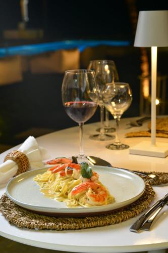 a plate of pasta with shrimp on a table with wine glasses at Pe na Areia Boutique Hotel in Japaratinga