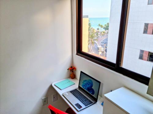 un ordinateur portable assis sur un bureau à côté d'une fenêtre dans l'établissement Maceio Ferias apto com varanda vista mar, à Maceió