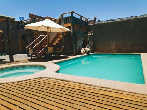 a swimming pool with an umbrella next to a wooden deck at La Casa de José in San Pedro de Atacama