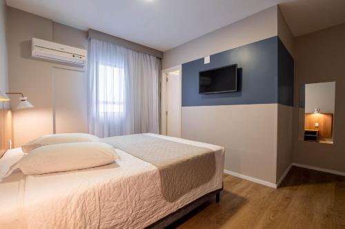 1 dormitorio con 1 cama y TV en la pared en Hotel Italia, en Balneário Camboriú