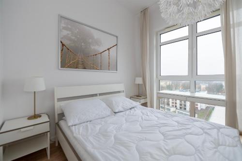een witte slaapkamer met een bed en een raam bij Penthouse with a View of Lodz & Free Parking in Łódź