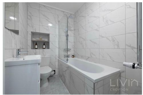 a white bathroom with a tub and a toilet and a sink at Lovely 1 Bedroom Apartment in South Norwood