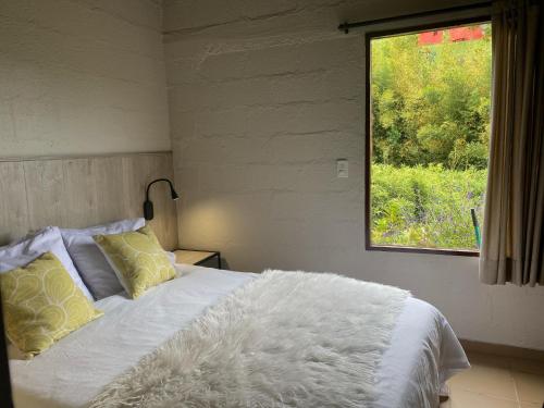 1 dormitorio con 1 cama blanca y ventana en Ecolodge Bahia del Peñón, en Guatapé
