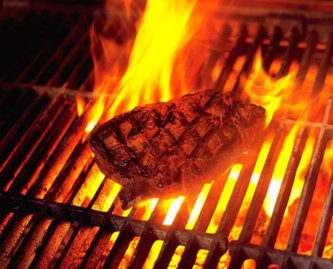 a steak is cooking on a grill with flames at Hotel Deutsches Haus Restaurant Olympia in Magdeburg