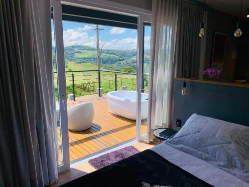 a bedroom with a tub and a balcony with a view at Vista Vigneti Albergo & Vino - Vale dos Vinhedos in Bento Gonçalves