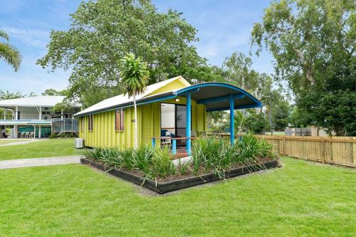 a small yellow house with a blue roof in a yard at Bali Hai Child Free Holiday Park Mission Beach in Mission Beach