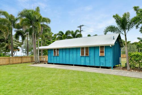 a blue house in a yard with palm trees at Bali Hai Child Free Holiday Park Mission Beach in Mission Beach
