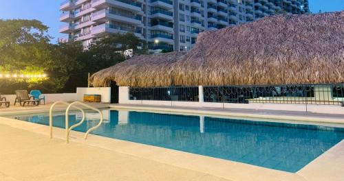 a swimming pool with a thatch roof at Hotel Los Veleros Santa Marta in Santa Marta