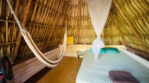 a hammock in a straw hut with a bed in it at Calypso cabanas in El Paredón Buena Vista
