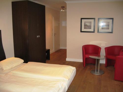 a bedroom with a bed and two red chairs at Hotel Kiose in Wenningstedt
