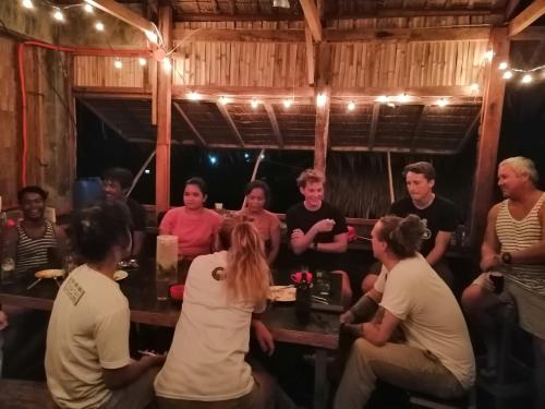 a group of people sitting around a table in a room at Titaays Surfers Inn in Baras