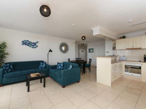 a living room with two blue couches and a kitchen at Seascape - Hosted by Burleigh Letting in Gold Coast