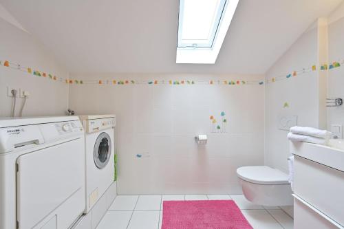 een witte badkamer met een wasmachine en een roze kleed bij Ferienwohnung Landhaus Helga unterm Schloss in Schwangau