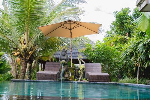 a statue of a monkey sitting under an umbrella next to a pool at Mancur Guesthouse in Ubud