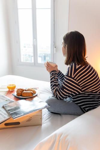 a woman sitting on a bed holding a cup of coffee at La Marinière Hôtel Restaurant in Saint Malo