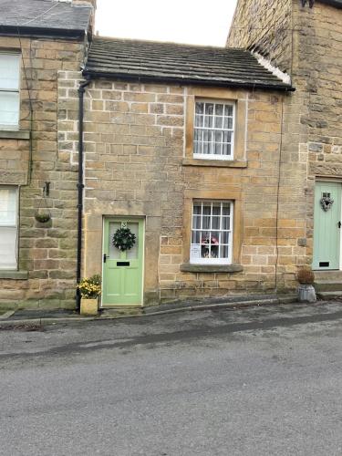 a brick house with green doors and windows at Carr’s cottage Eyam Peak District, in Eyam