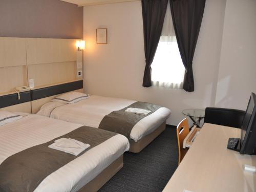 a hotel room with two beds and a desk at KOKO HOTEL Numazu Ekimae in Numazu