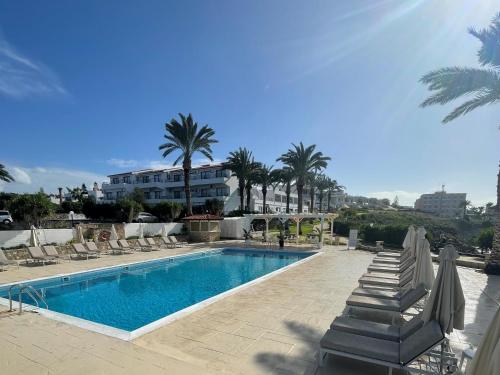 a swimming pool with lounge chairs and palm trees at Vrachia Beach Hotel & Suites - Adults Only in Paphos City