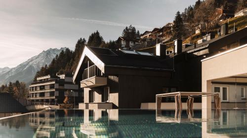 a building with a swimming pool in front of a mountain at Hotel Sunshine Superior "ADULTS ONLY" Ischgl - Kappl in Kappl