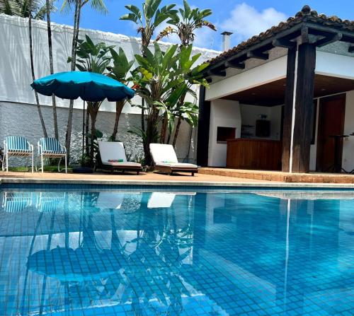 a swimming pool with two chairs and an umbrella at Pousada Casa Paradiso Guarujá in Guarujá