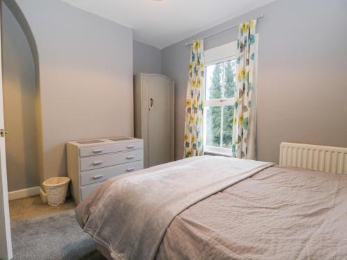 a bedroom with a bed and a dresser and a window at 7 Railway Cottages in Ulverston
