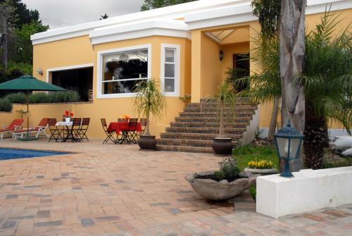 a yellow house with a patio with tables and chairs at Big6 Guesthouse in Somerset West