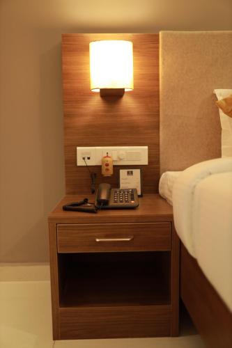 a night stand with a phone and a lamp on a bed at Hotel Kottayam Grand in Kottayam