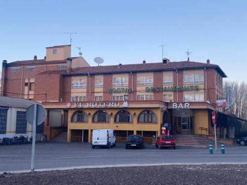 un grand bâtiment en briques avec des voitures garées devant lui dans l'établissement Hostal El Botero, à Monreal del Campo