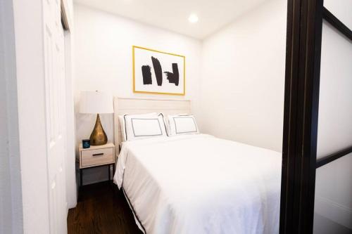 Dormitorio blanco con cama y mesa con lámpara en 69-3C Stylish Lower East East 1br Apt BRAND NEW, en Nueva York
