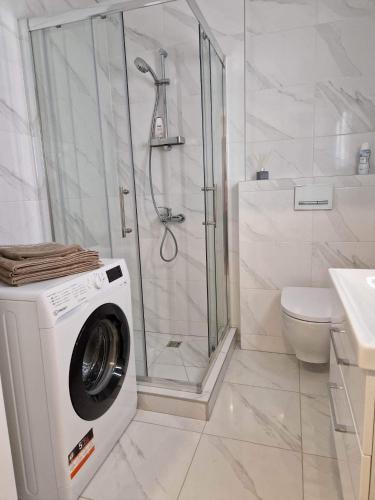 y baño blanco con ducha y lavadora. en Parko nauji apartamentai, en Panevėžys