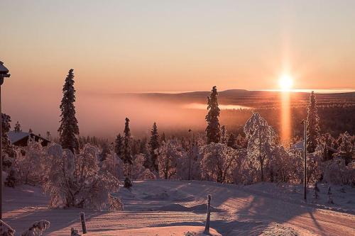 a sun setting over a snow covered slope with trees at Tupasvilla in Saariselka